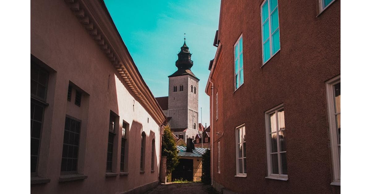 A narrow alley in Visby's Old Town, with the tower of St. Mary's Cathedral visible between the building facades.