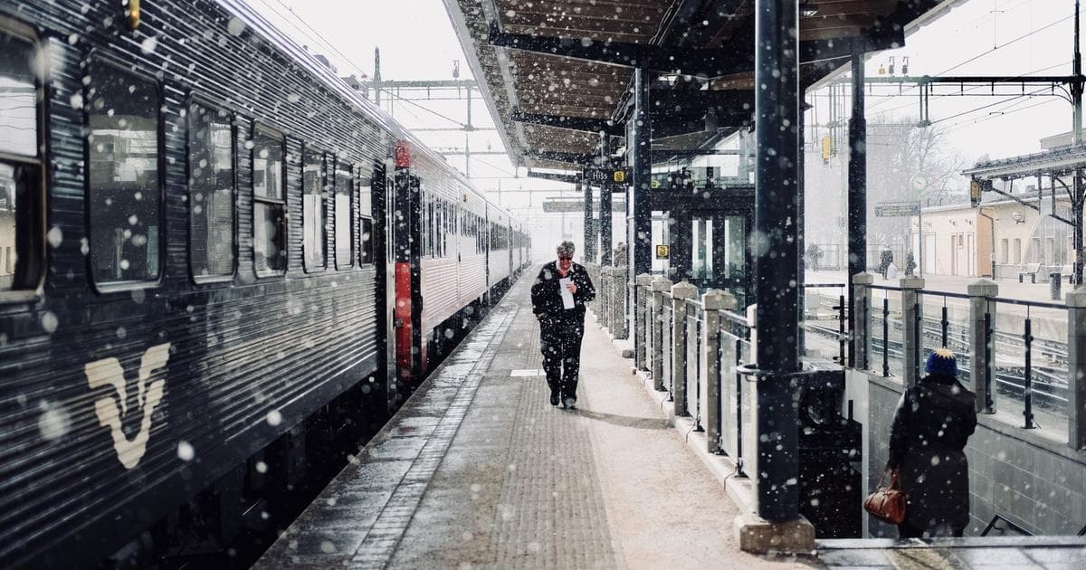 A traveler walking along a railway platform beside a passenger train, suitcase in hand.