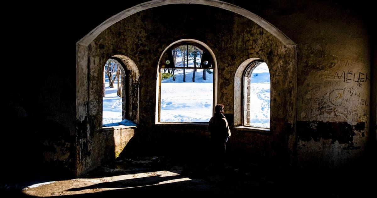 Person looking out an arched window at a snowy winter landscape