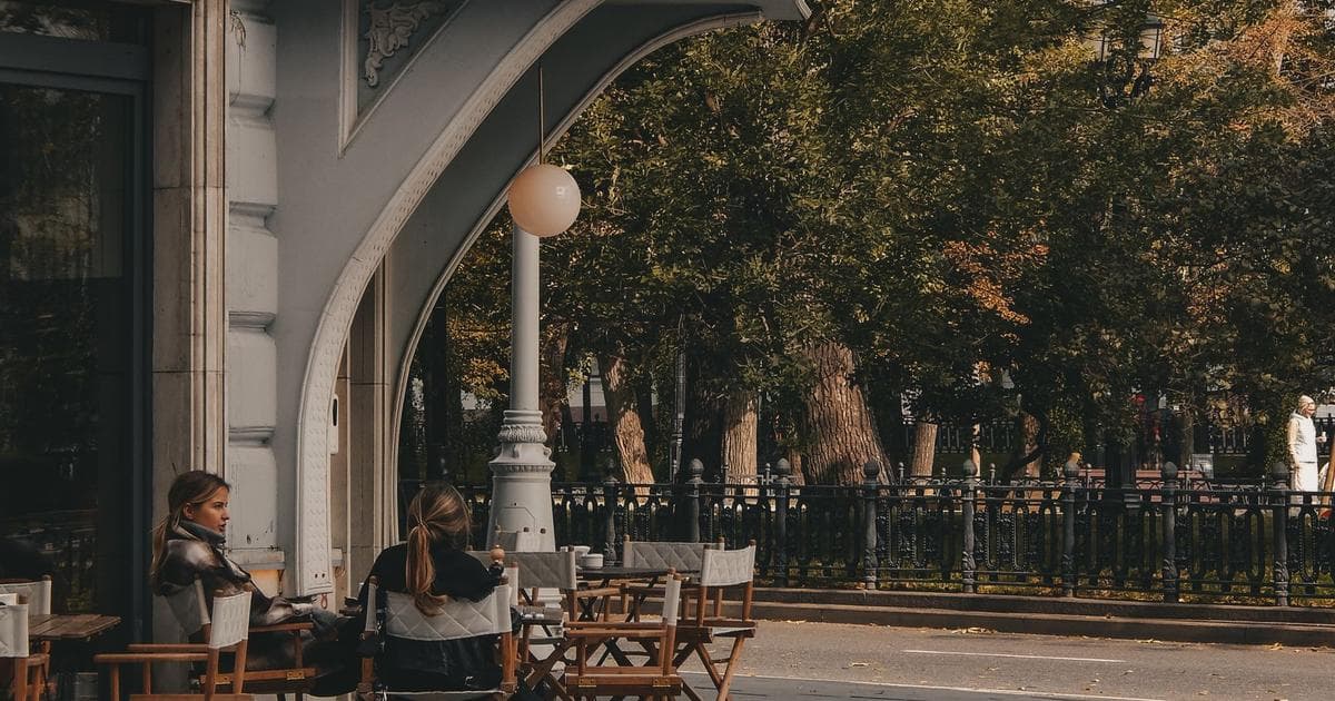 Two people talking at an outdoor café table in autumn light